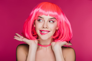 beautiful girl biting lip and posing in neon pink wig, isolated on pink