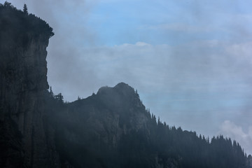 Fog in hight mountain landscape. Overhanging cliffs with tree.