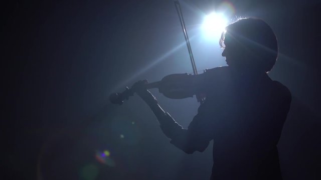 Dark scene with a violinist she bows on strings glare around the room. Black smoke background. Back view