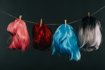 four colorful wigs hanging on rope isolated on black