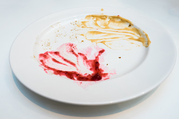 High angle view of dirty white plate with red and yellow souce on white background. dirty and empty dish.
