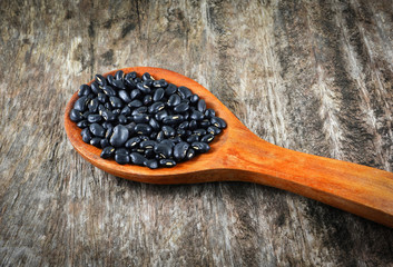 Black bean on wooden spoon grain seeds on old wood background