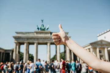 A person shows a sign with a finger upwards meaning everything is okay or confirms against the background of the Brandenburg Gate and blurred unrecognizable people in Berlin in Germany.
