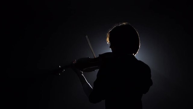 Musician girl backs to the camera playing the violin . Black smoke background. Back view