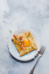 Crepe with fried egg, cheese, bacon and green onions for breakfast on a light gray concrete background.