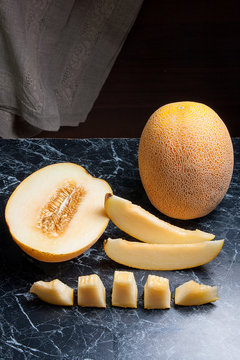 Whole, half and sliced honeydew melon fruit on dark marble background.