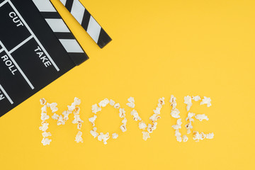 clapperboard and "movie" lettering made with popcorn isolated on yellow