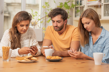 Friends sitting in the kitchen and watching on their phones