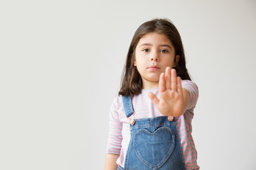 Little serious Hispanic girl making stop gesture. Adorable kid gesturing forbidden with one hand. Isolated on white. Prohibition concept - obrazy, fototapety, plakaty