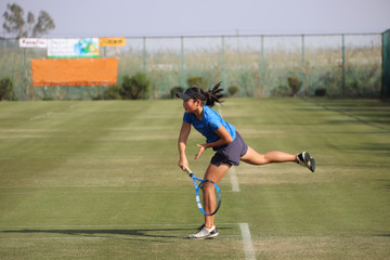 天然芝のコートでサーブ打つジュニアテニスプレイヤー