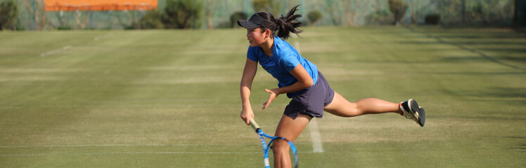 天然芝のコートでサーブ打つジュニアテニスプレイヤー