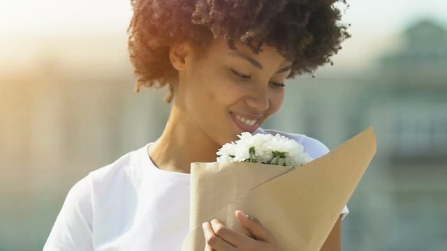 Happy afro-american woman sniffing flowers aroma and smiling, enjoying present