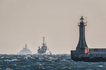 MARITIME TRANSPORT - Tugboat and warship on foamy waves roadstead of the port in Gdynia