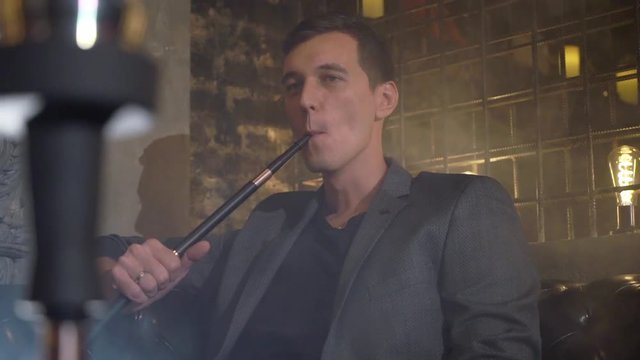Hookah smoker. Young man smoking shisha or hookah in cafe or bar. Resting in shishabar lounge.