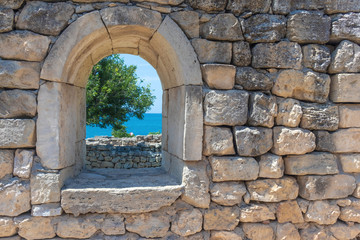 wall with a window in the ruins of the ancient city with a view of the sea, a tree and people, selective focus