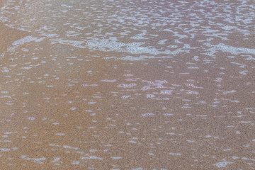 Texture of the remains of a foamy wave on the beach, abstract background