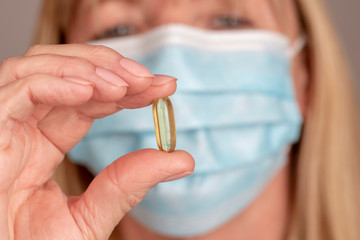 Woman wearing a mask holding a prescibed capsule between her thumb and forefinger.