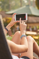 Girl using cellphone while lying on a swimming pool deck lounge bed.