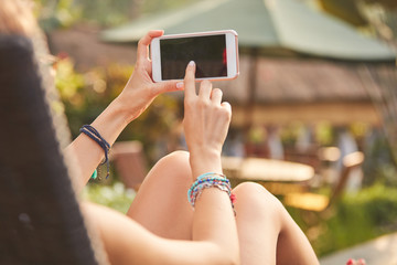 Girl using cellphone while lying on a swimming pool deck lounge bed.