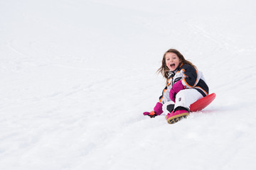 Blond girl playing on snow sliding and laughing at resort, with copy space