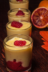 Vier Dessertgläser in Reihe mit Vanillecreme, Himbeere und Blutorange, low key vertikal