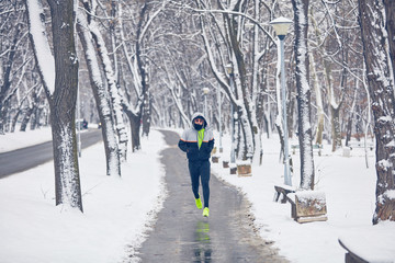 Man jogging in snowy park and cold weather.