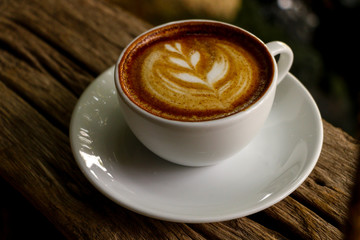 Hot cofffee cup on wooden with painting leaf