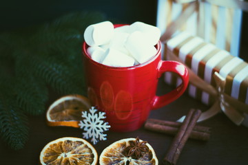 Red cup of coffee or hot chocolate with marshmallow on wooden dark background. Cinnamon sticks, stars with bokeh. Winter concept. Hot coffe with marshmallow.