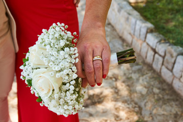 A couple holding a wedding bouquet in front of them, man in white and woman in red dress ring on finger.