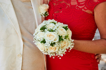 A couple holding a wedding bouquet in front of them, man in white and woman in red dress.