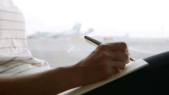 Young woman writing in diary at airport, close-up in slow motion