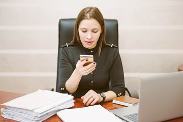 Business woman looking at the mobile. Successful business lady lawyer is sitting at her work place. Happy business woman working in office with documents.