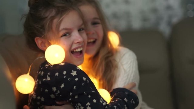 Pajamas party, two girlfriends schoolgirl fooling in the evening in bed. Christmas evening, illumination, sisters in the bedroom