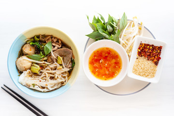Spicy rice noodles soup in a bowl with chopsticks and ingredients, Asian food