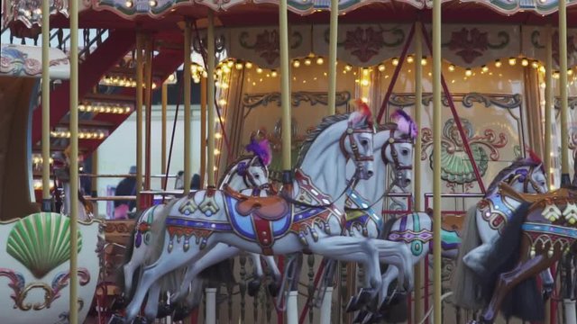 Slow motion shot of vintage, colorful merry go round carousel horses turning and moving up and down in the evening in an urban illuminated christmas setting.