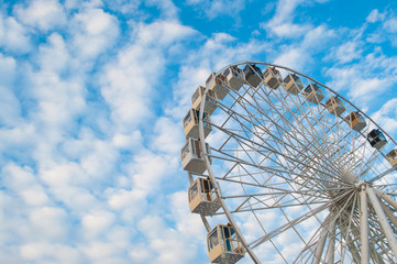 Part of ferris wheel over blue cloudy sky background in a fun park.