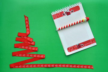 Christmas tree made of red ribbon, notebook with handle in the form of a snowman on green background