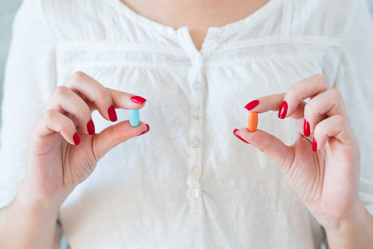 woman in white holding red and blue pills. medication treatment and health