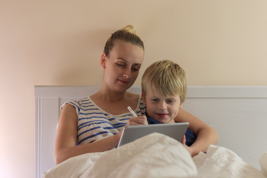 Beautiful Mom And Her Son Lie On The Bed And Watching In Tablet