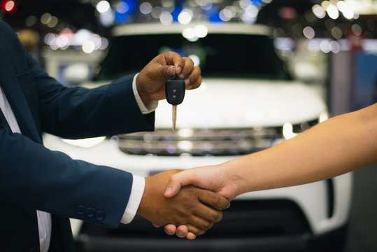 Handshake Of Two Businessmen When Selling A Car In A Motor Show, Auto Business, Car Sale, Deal, Gesture And People Concept - Close Up Of Dealer Giving Key To New Owner And Shaking Hands In Showroom.