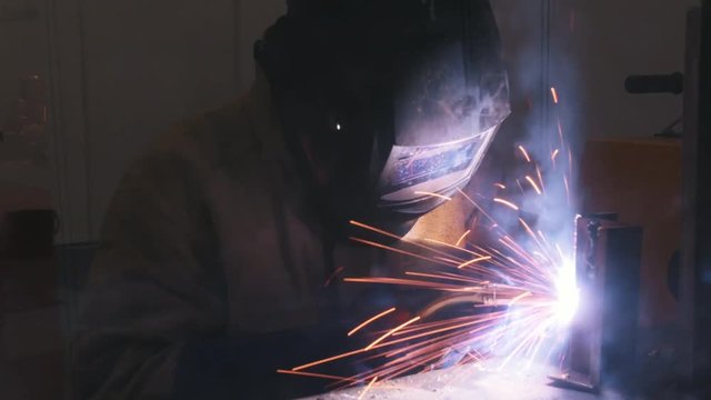 Welding process. A welder in helmet doing his job in the dark. Smoke and sparks