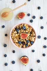 Pink bowl of fruit granola with fruits and honey, overhead view. Flat lay, from above, top view. Closeup.