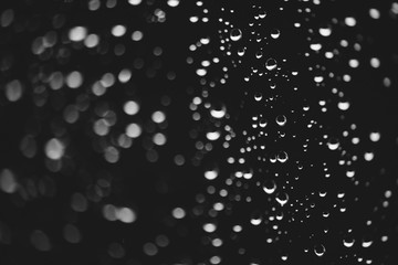 Dirty window glass with drops of rain. Atmospheric monochrome dark background with raindrops in bokeh. Droplets and stains close up. Detailed transparent texture in macro. Copy space. Rainy weather.