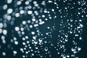 Naklejka na ściany i meble Dirty window glass with drops of rain. Atmospheric blue background with raindrops in bokeh. Droplets and stains close up. Detailed transparent texture in macro with copy space. Rainy weather.