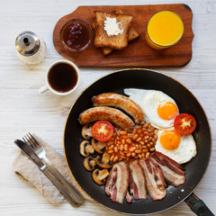 Full English breakfast in a pan with fried eggs, bacon, sausages, beans and toasts on white wooden surface, top view. Flat lay. From above, overhead.