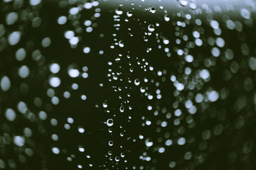 Dirty window glass with drops of rain. Atmospheric green background with raindrops in bokeh. Droplets and stains close up. Detailed transparent texture in macro with copy space. Rainy weather.
