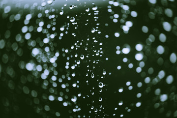 Dirty window glass with drops of rain. Atmospheric green background with raindrops in bokeh. Droplets and stains close up. Detailed transparent texture in macro with copy space. Rainy weather.