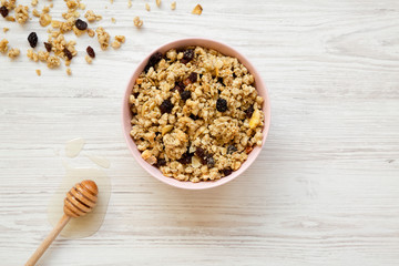 Pink bowl of fruit granola and honey over white wooden surface, overhead view. Copy space.