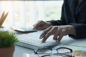 A businesswoman analyzing investment charts at his workplace and using his laptop and touch calculator.