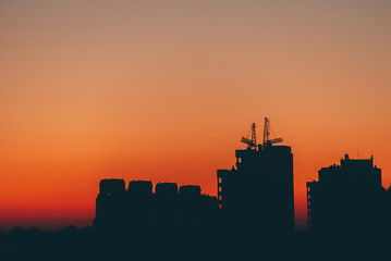 Cityscape with vivid fiery dawn. Amazing warm dramatic cloudy sky above dark silhouettes of city...